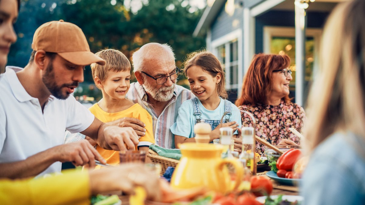 Elderly man sits at a table with grandchildren in his lap, surrounded by other family.