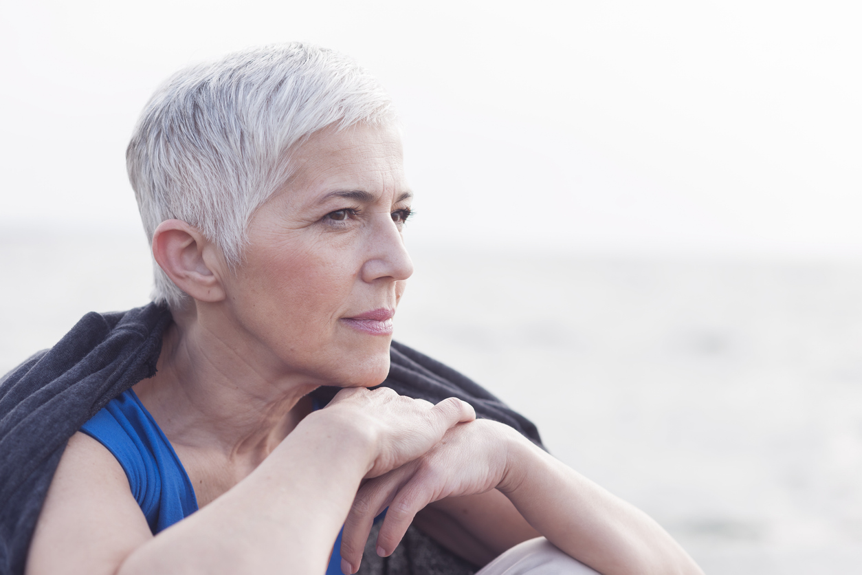 Senior woman at coast, sitting and looking at the sea.