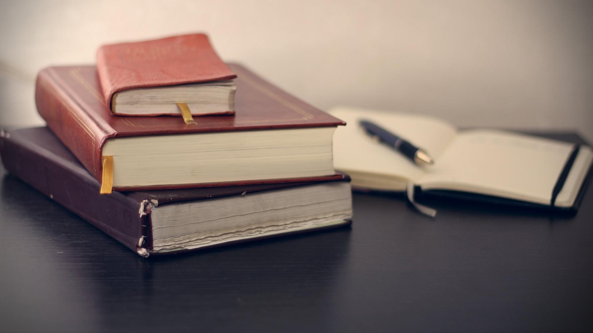 Libros sobre una mesa y un cuaderno abierto con un bolígrafo encima.