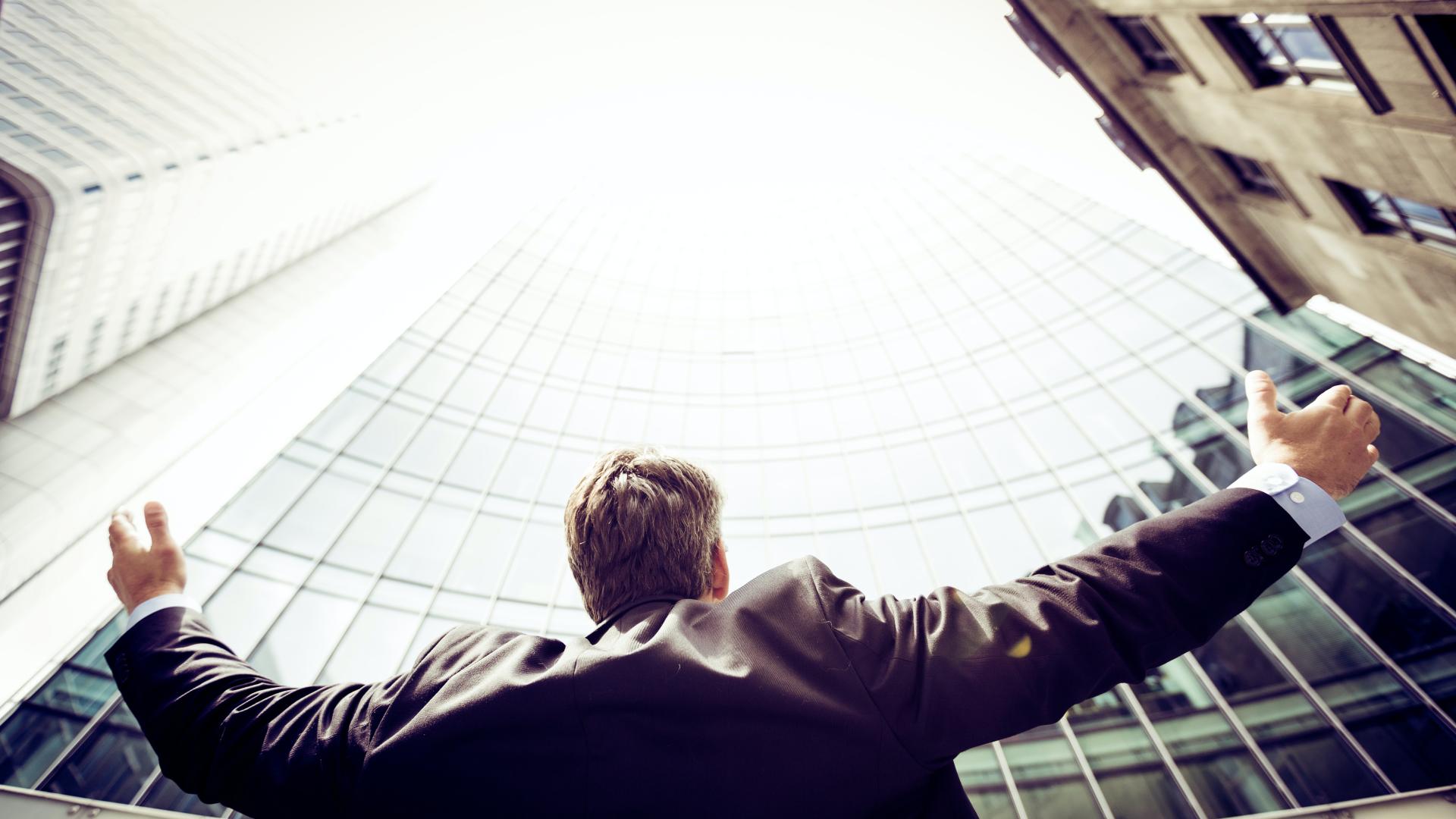 Man reaching out arms and looking up at tall city buildings.