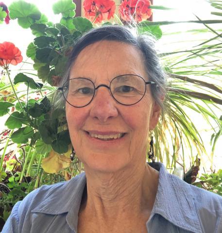 Woman wearing glasses with plants and flowers in the background.