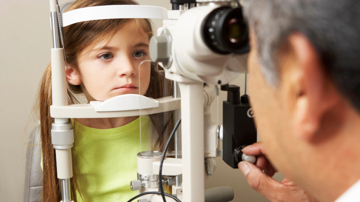 Male Optician In Surgery Giving Young Girl Eye Test