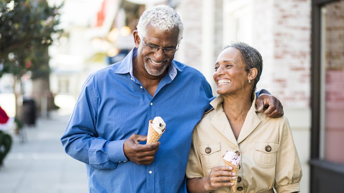 An older African American couple walks happily outdoors, each holding an ice cream cone.