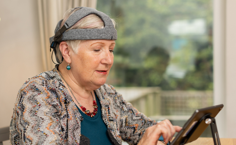 An older woman wearing a device on her head and holding a tablet. 