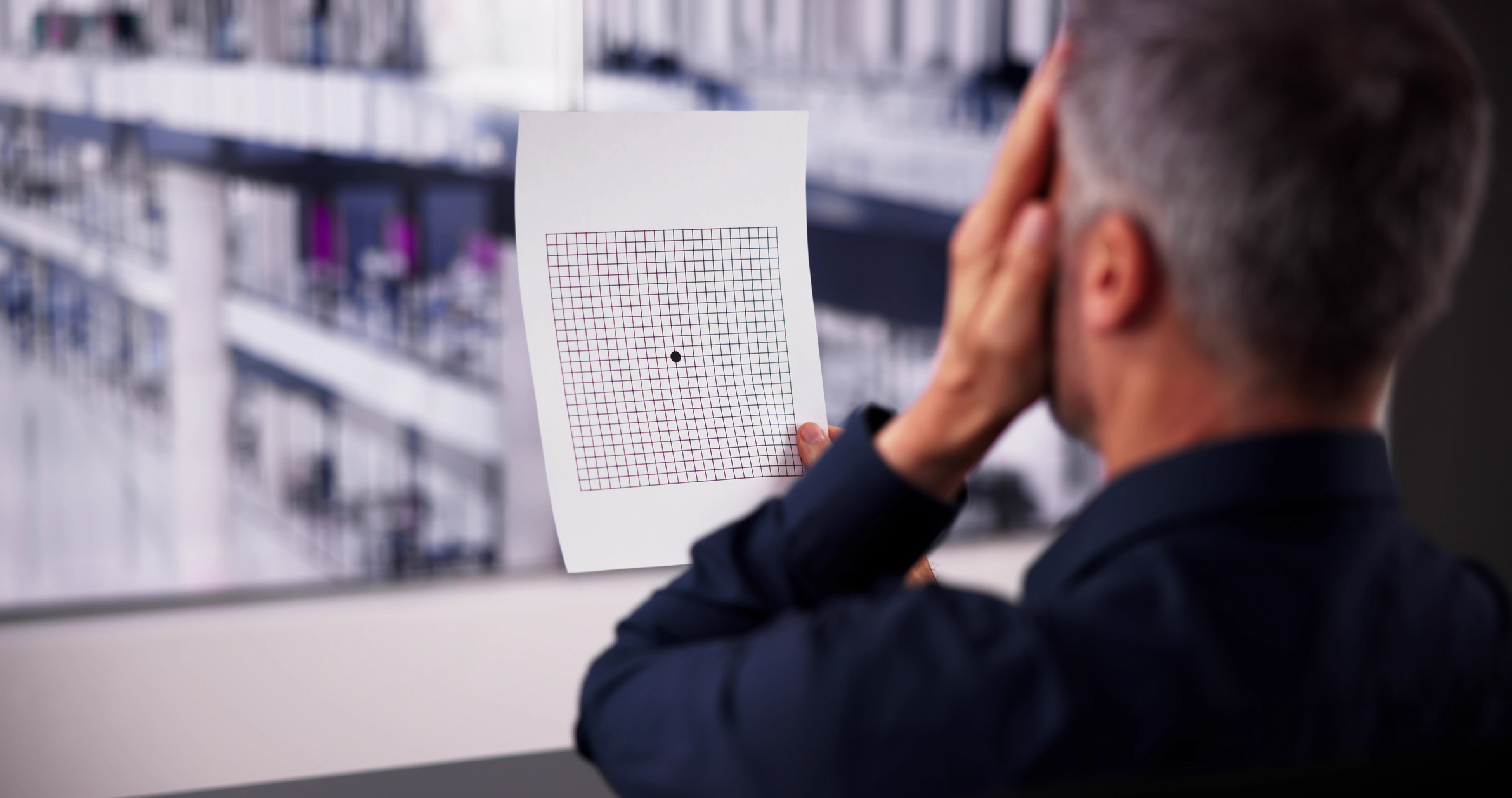 Man covers his left eye while using the Amsler gird printed on a piece of paper as a form of at-home macular degeneration testing.