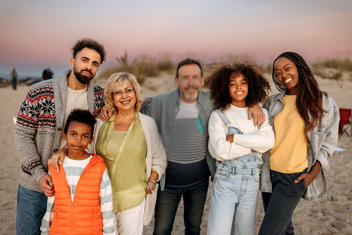 The same family on the beach at sunset, with all faces clearly visible except for the man in the middle, whose face is still partially blurred. The rest of the family is smiling at the camera.