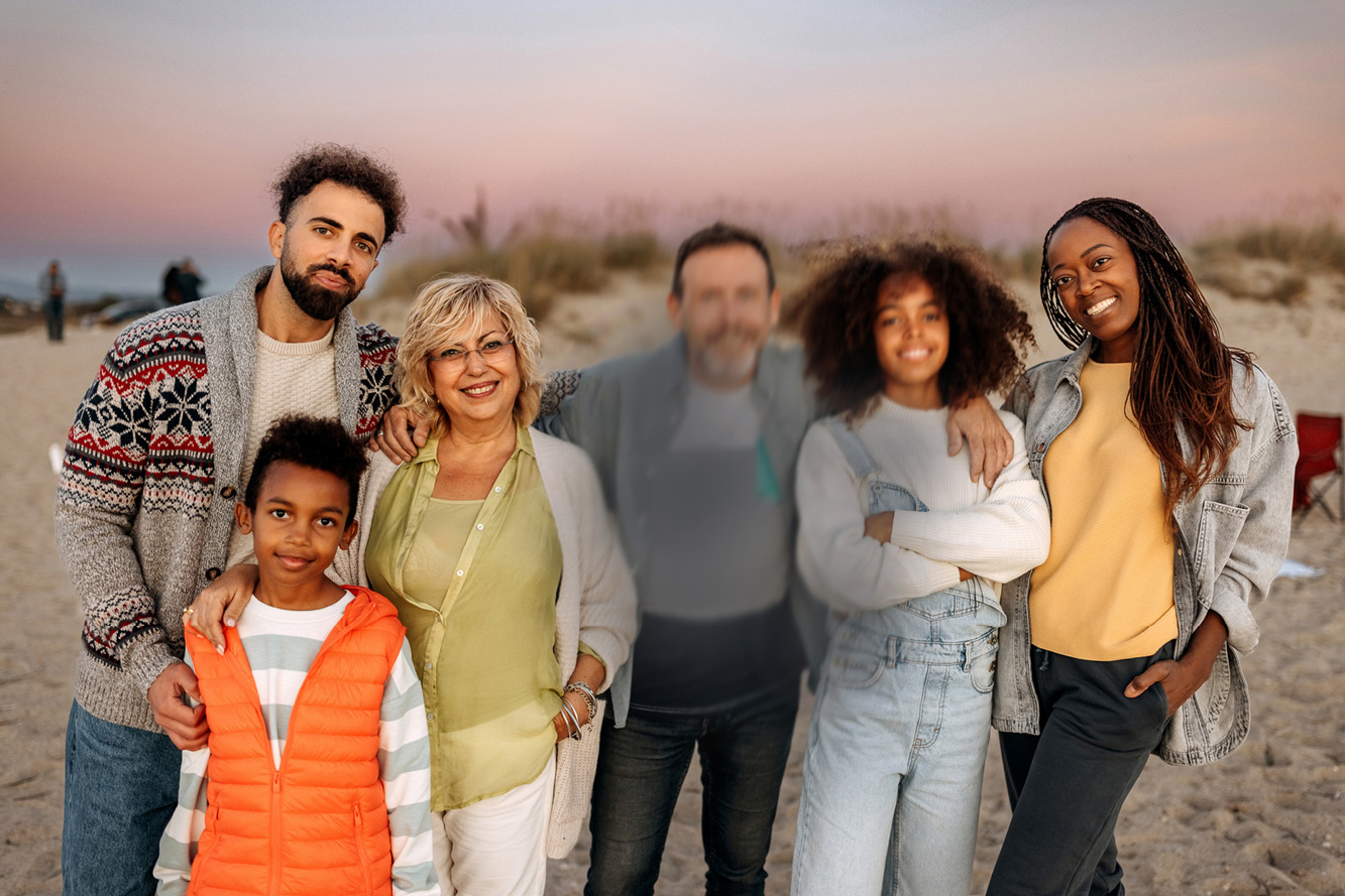 The family stands together on the beach at sunset, with all faces visible except for the man in the middle, whose face is partially blurred.