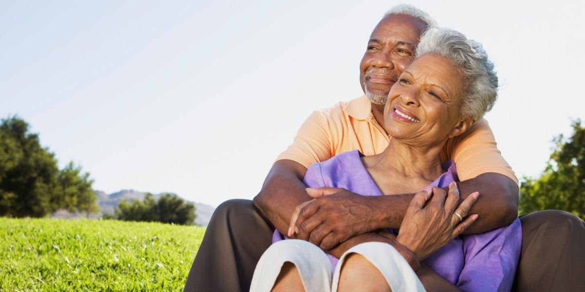 Smiling elderly couple sitting outdoors embracing on a sunny day.