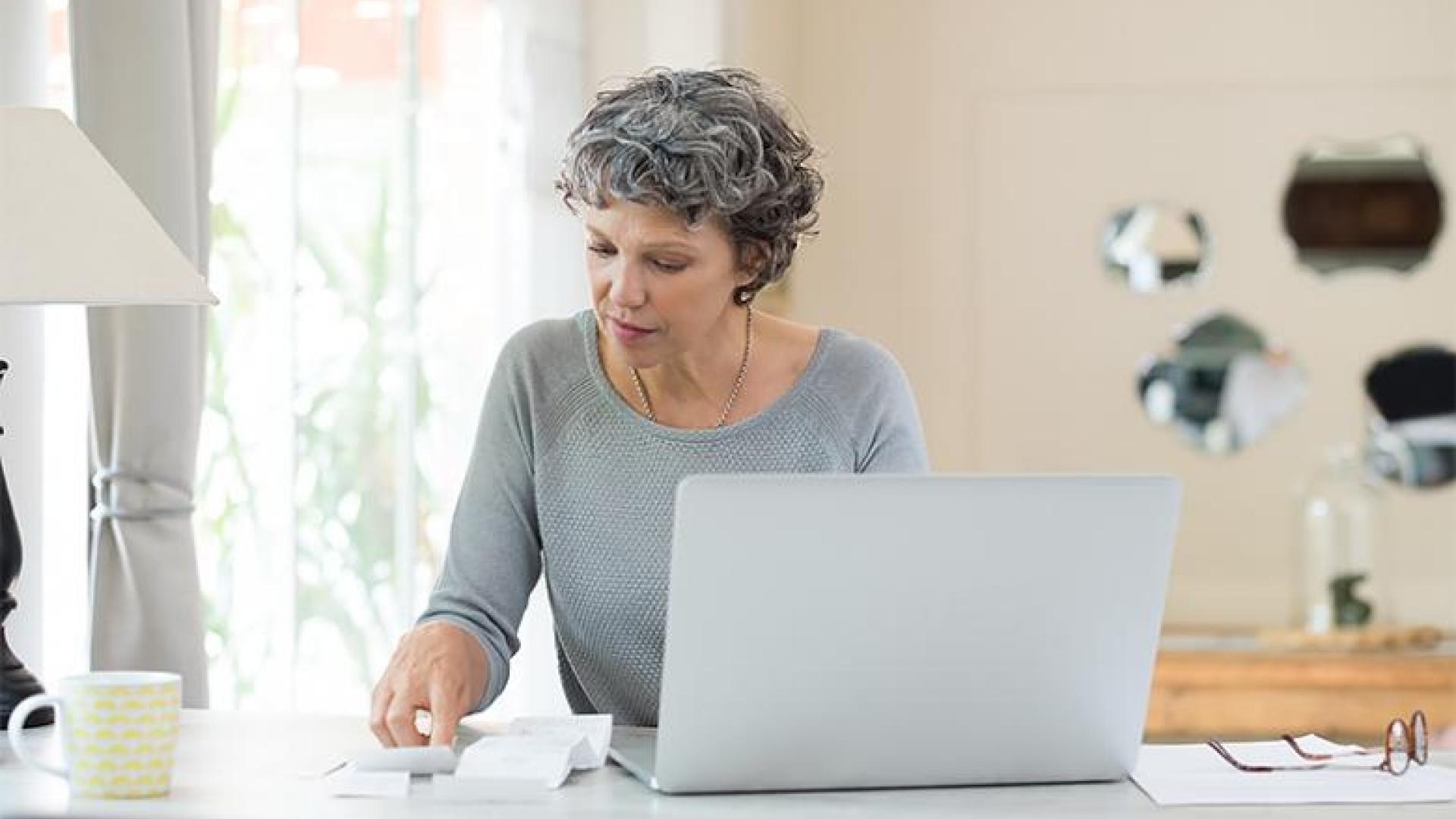 Woman using laptop and pen and paper to manage finances.