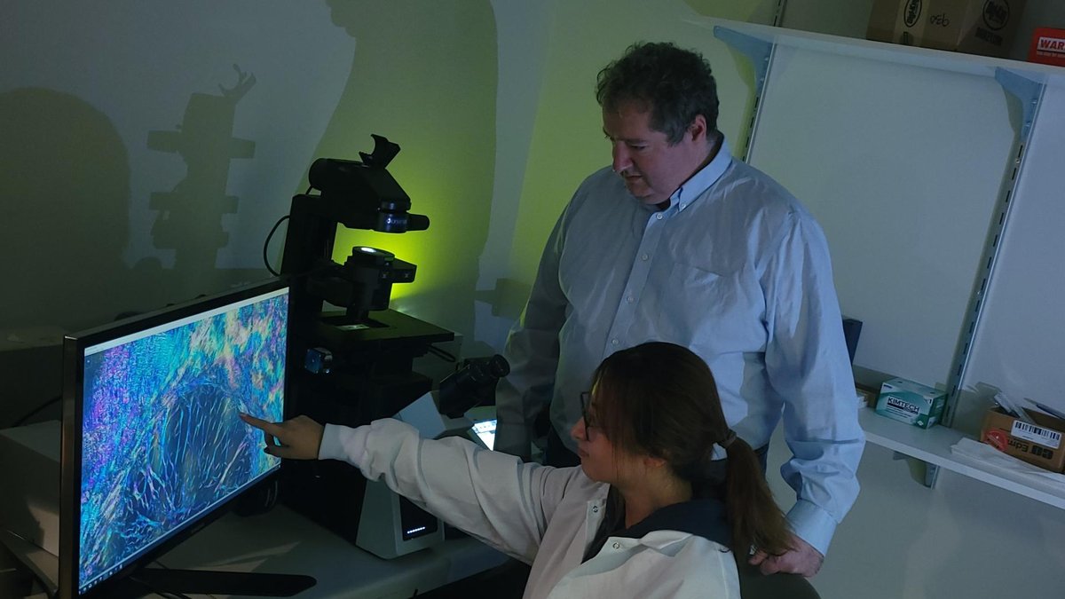 A lab researcher points at a colorful image on a computer screen, while a scientist stands next to her observing the data.