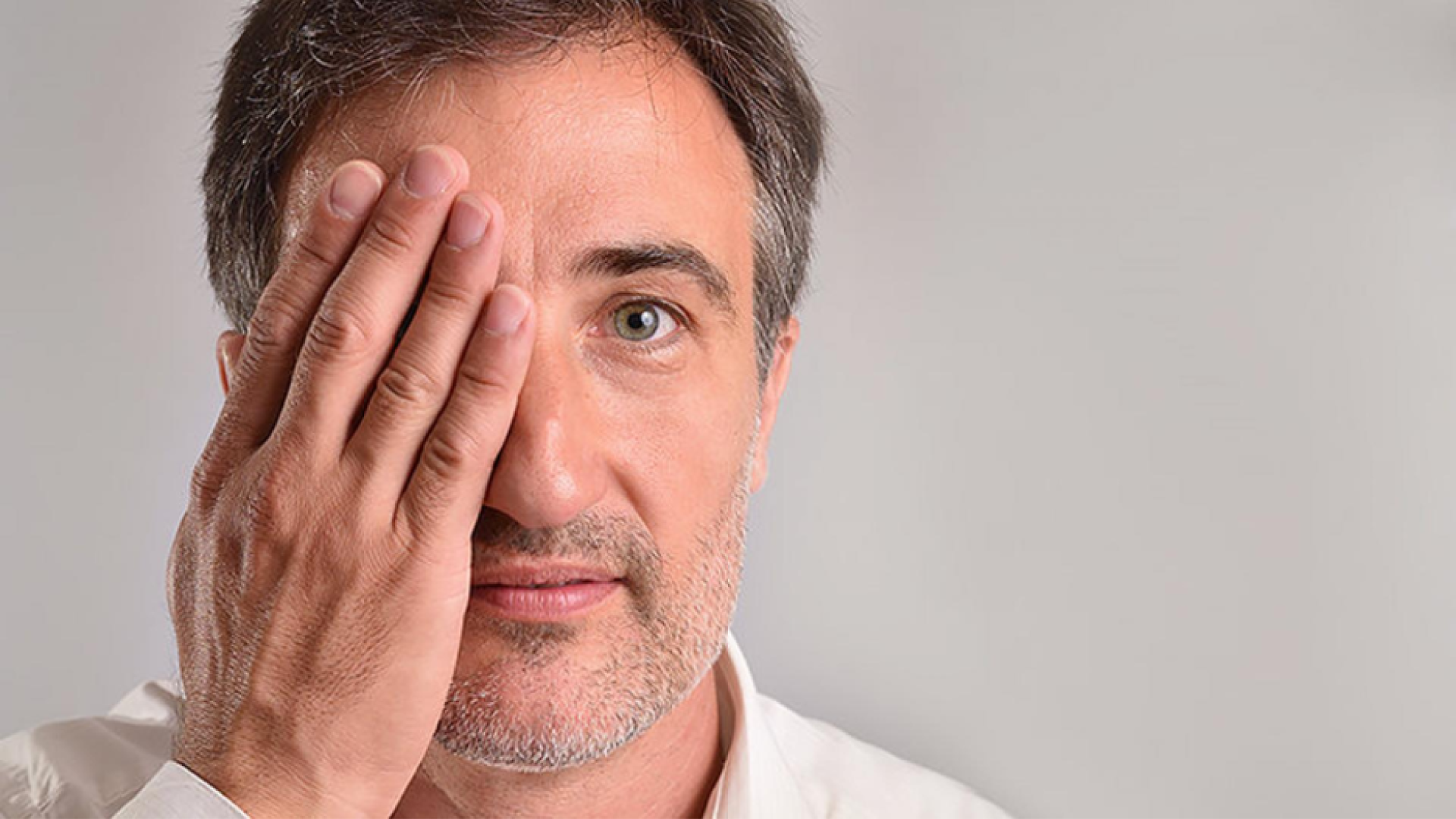 A photo of a man from the neck up. He has one hand over his right eye.