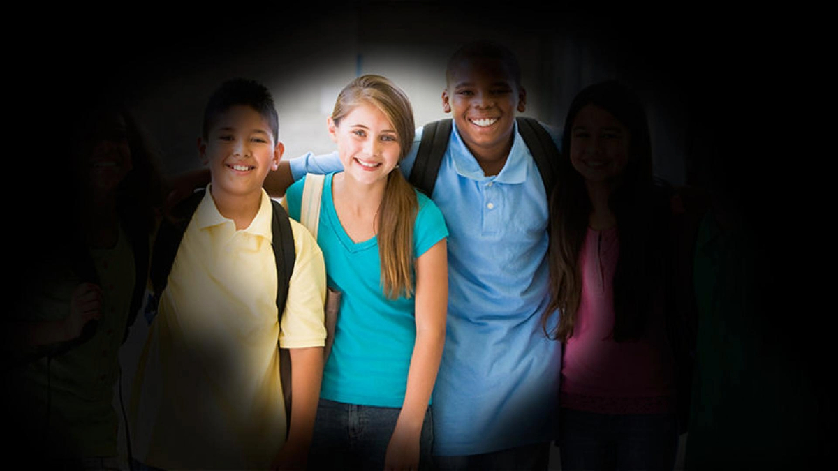 A group of four smiling students standing together, surrounded by darkness.