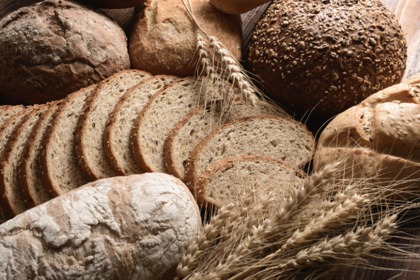 Assorted freshly baked breads including whole grain, rye, and sourdough, with wheat stalks on a wooden table.