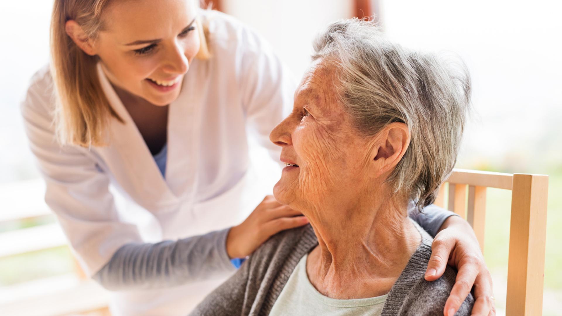 A caregiver happily smiling and greeting a senior woman.