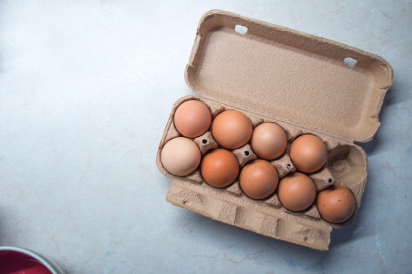 A carton of eggs is open, displaying ten brown eggs on a pale blue surface.