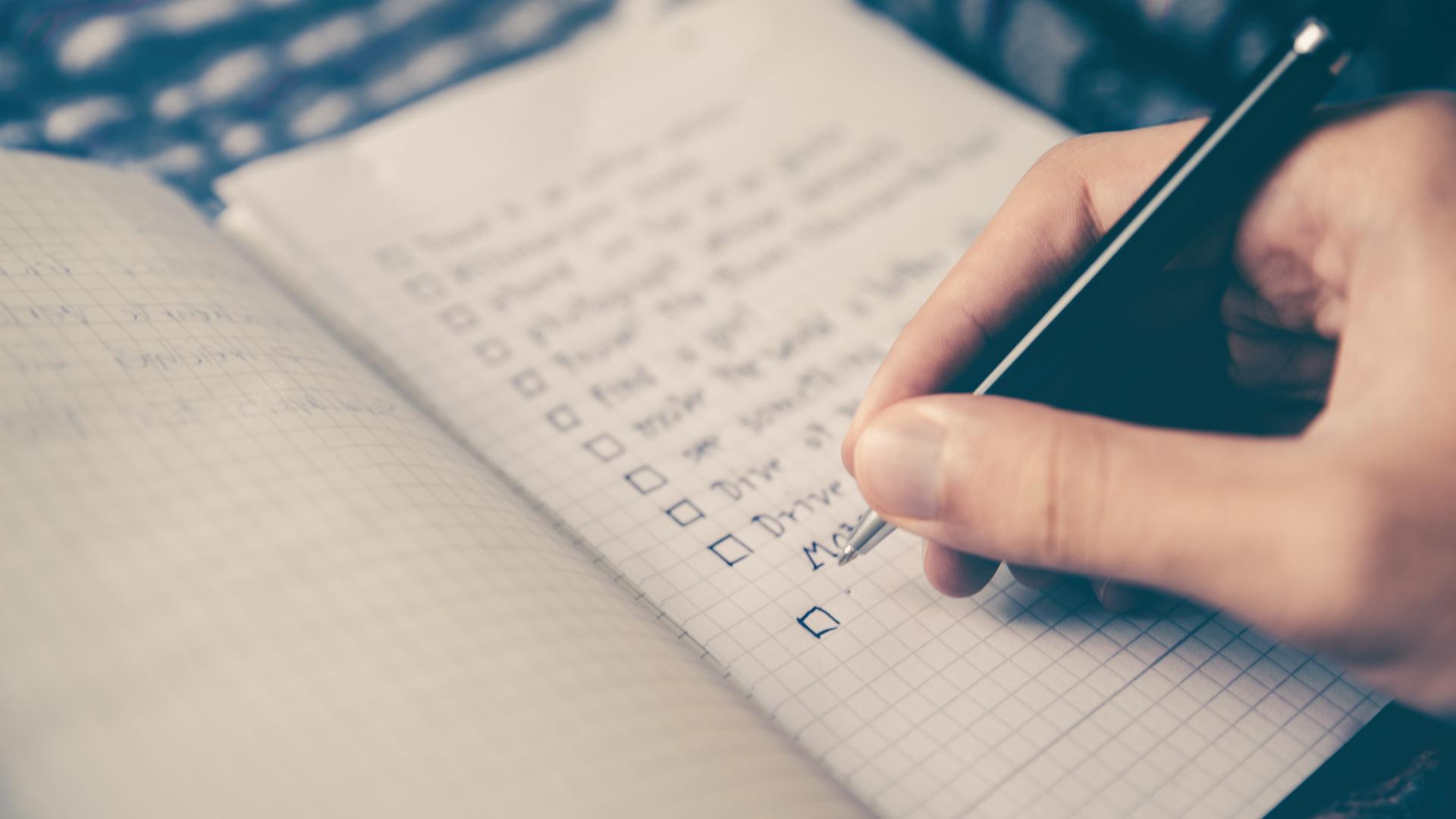 A photograph of someone's hand holding a pan to write on grid line paper. None of the words are in focus.