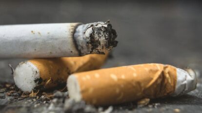 Close-up of three extinguished cigarettes with ash, one partially crushed, on a textured surface.