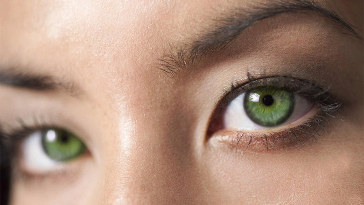 Close-up of a person with striking green eyes, highlighting detailed textures of the irises and eyelashes.