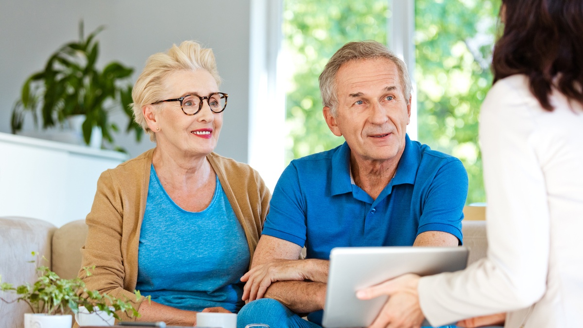 Senior couple sits together on a couch meeting with a financial professional.