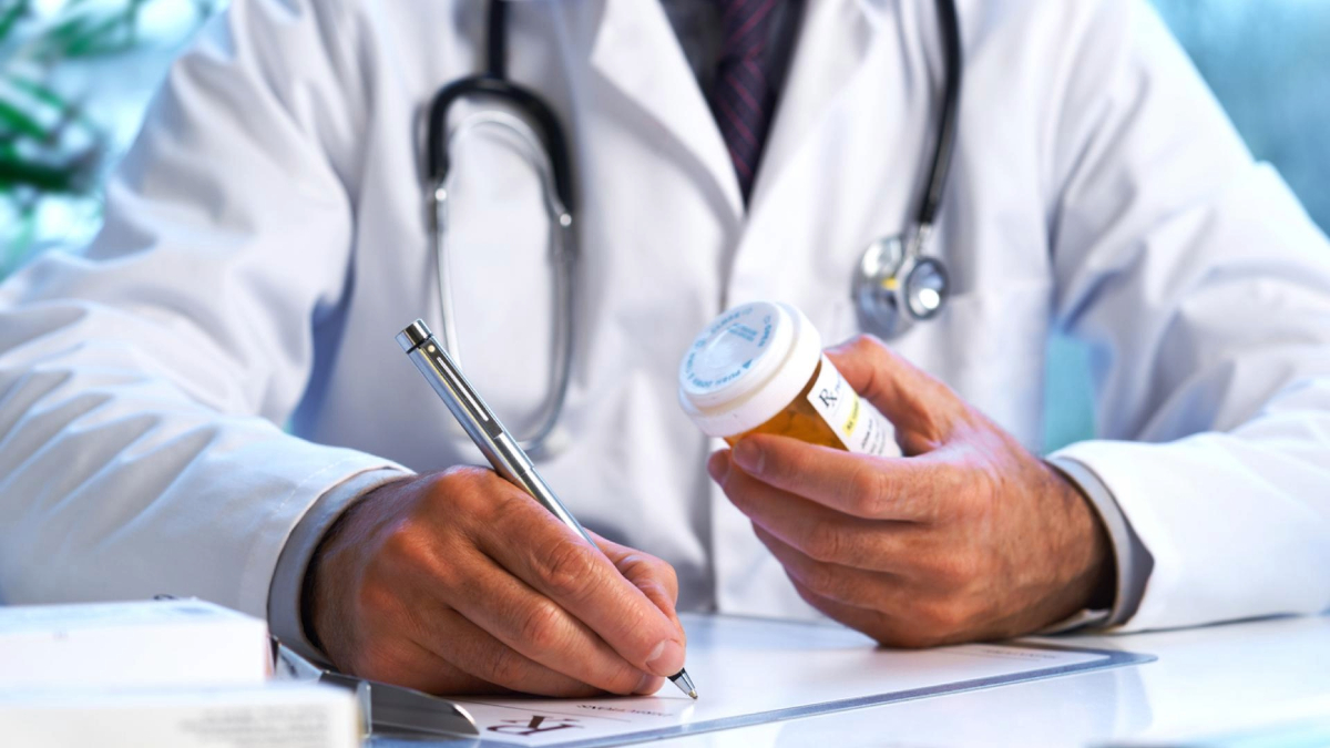 Doctor writing notes while holding container of prescription pills.