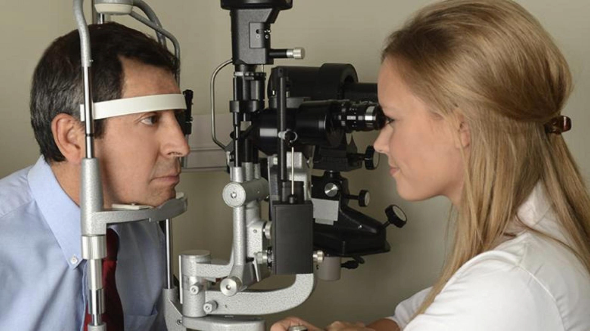 An optometrist conducts an eye examination on a patient using a slit lamp biomicroscope.