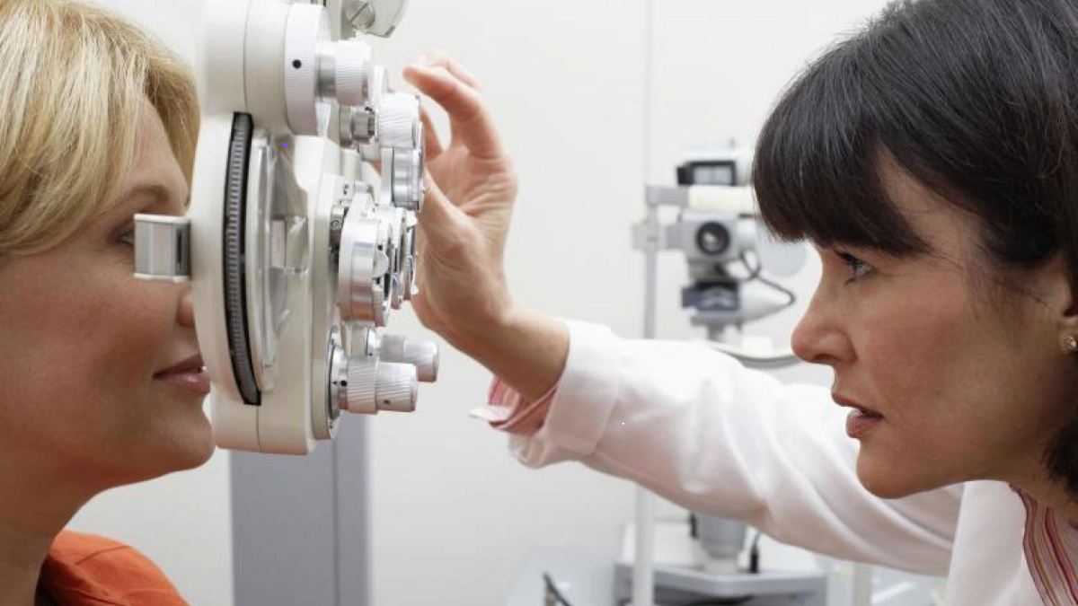 An optometrist adjusting an eye examination machine for a patient in a clinic.