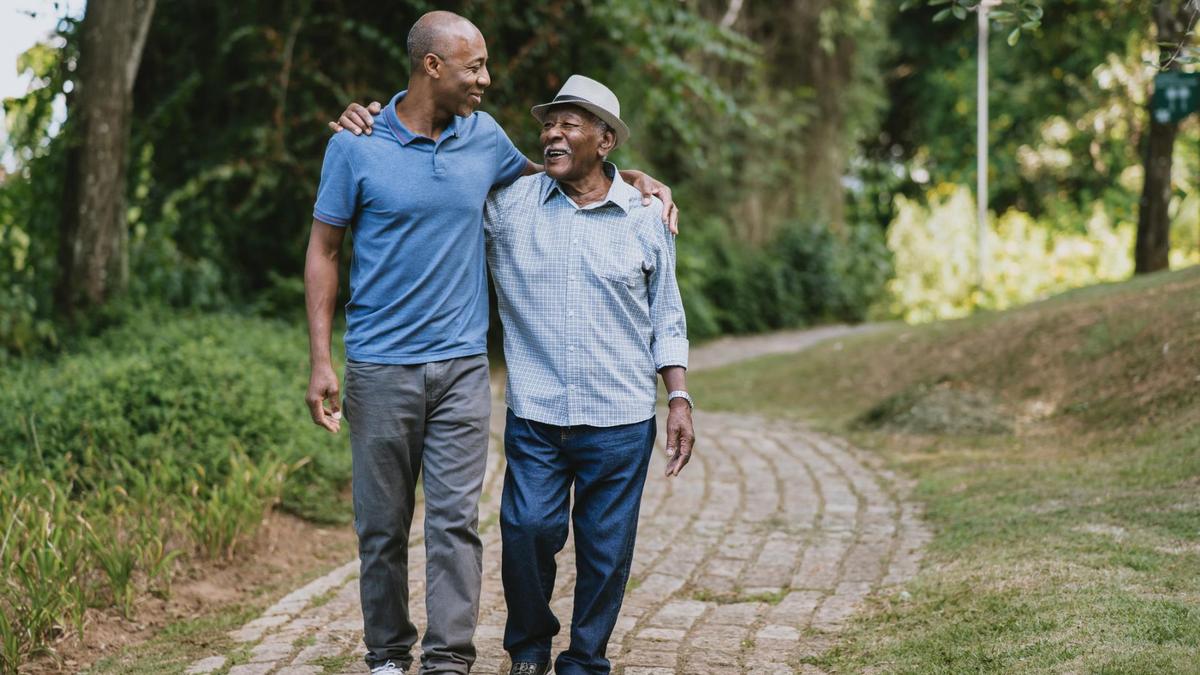 A father and son walking together outside on a paved path, sharing a moment of connection and joy, surrounded by greenery.