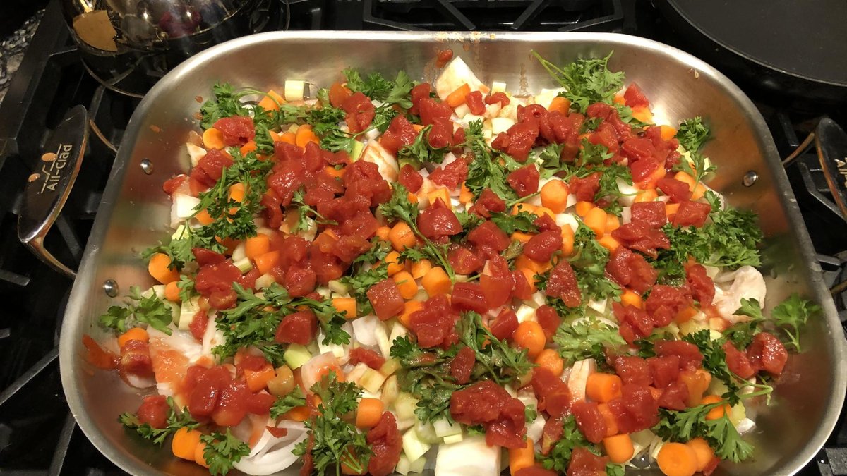 A pan filled with a vibrant mix of chopped carrots, parsley, onions, and tomatoes, ready to be cooked, sitting on a stovetop.