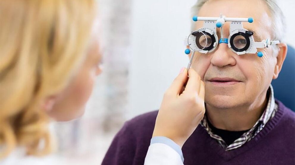 A man undergoing an eye exam with specialized glasses, as a healthcare professional adjusts the lenses.