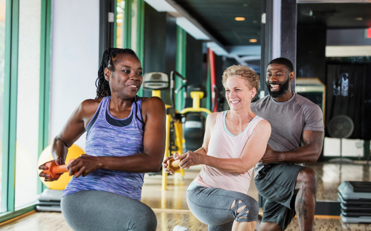 Three adults exercising with resistance bands in a gym, smiling and engaged in their workout.