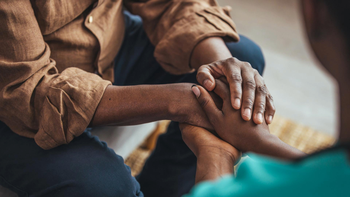 Two individuals sitting and holding hands in a comforting gesture.