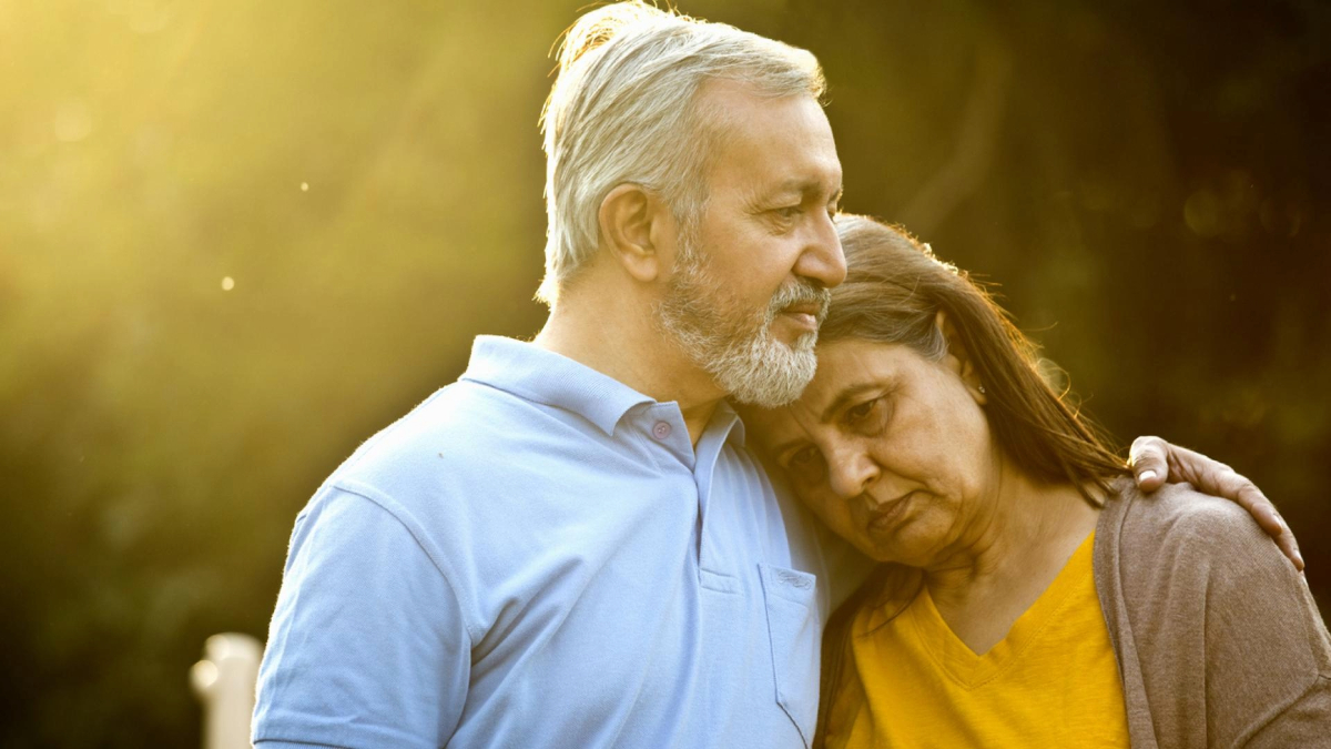 Two older adults embracing and sharing a tender moment in a sunlit outdoor setting.