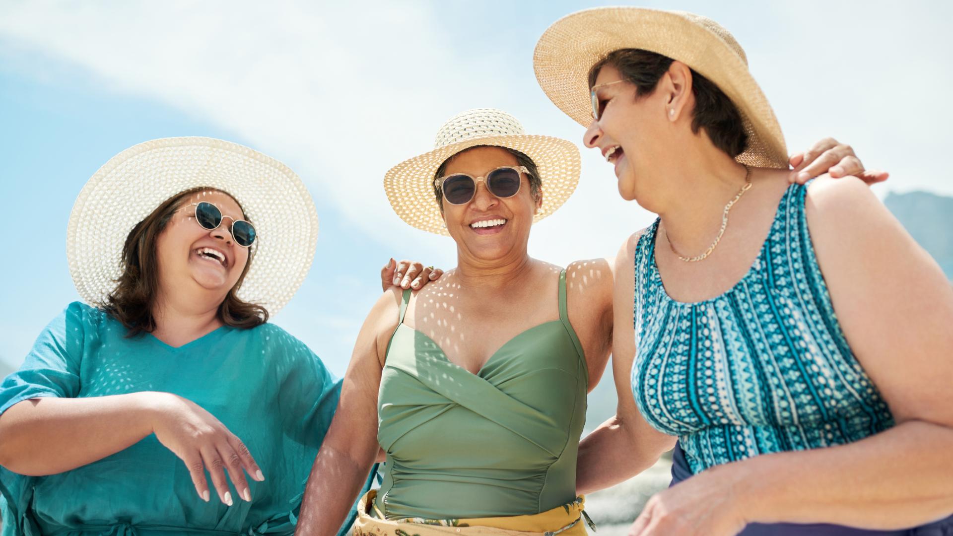 three women dressed in beachwear plus dark sunglasses and wide-brimmed sunhats