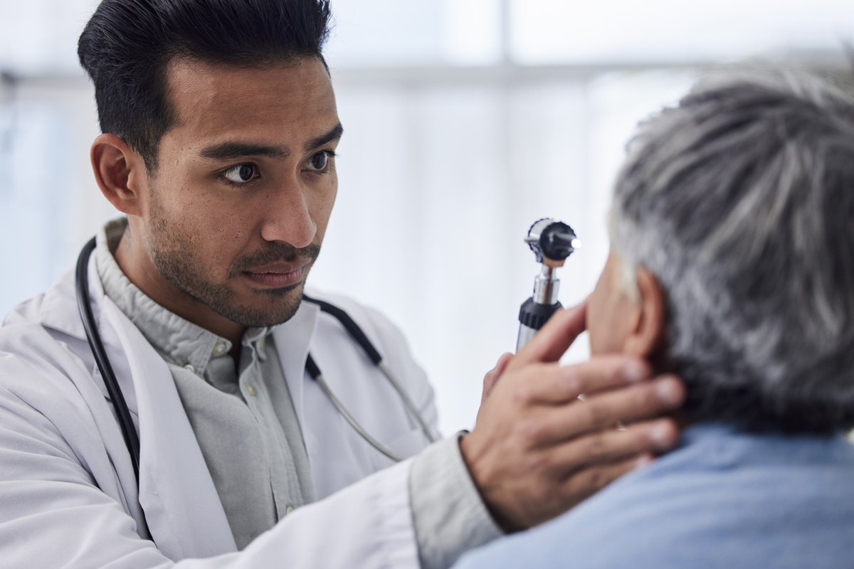 A doctor in a white coat examines a patient's eye with a specialized medical tool, focusing intently.