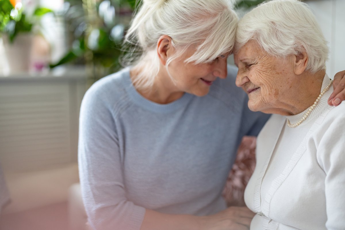 A touching moment between two elderly women with white hair, sitting close together.