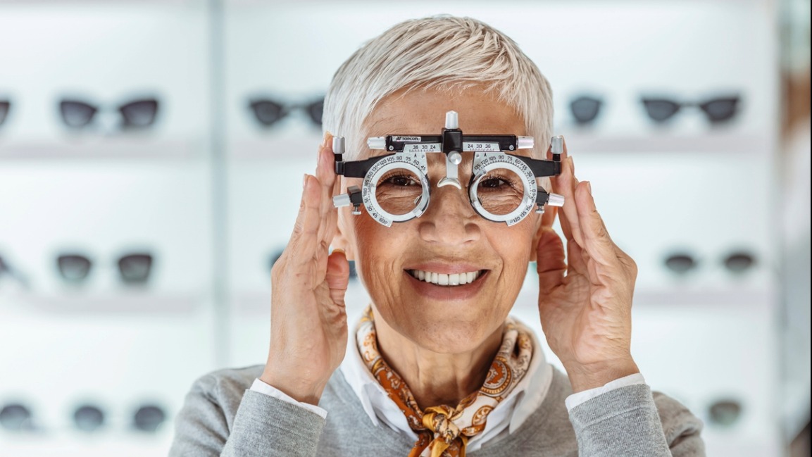 Person trying on glasses with a specialized trial frame at an optometrist's office, smiling, wearing a fashionable scarf.