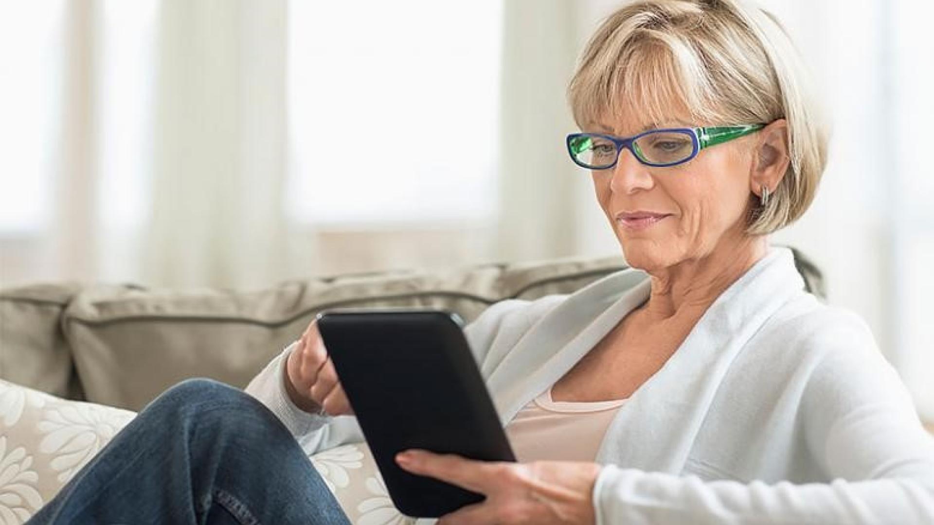 a woman sitting on a couch while reading from a tablet