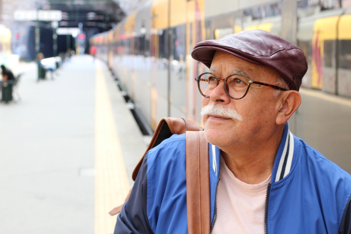 Man walking with backpack at train station, looking into the distance.