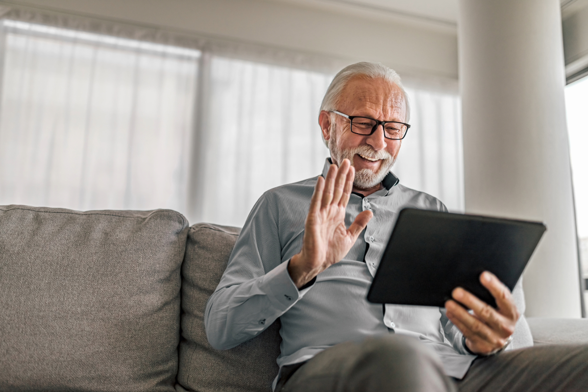 Person sitting on a couch, smiling and waving at a tablet.