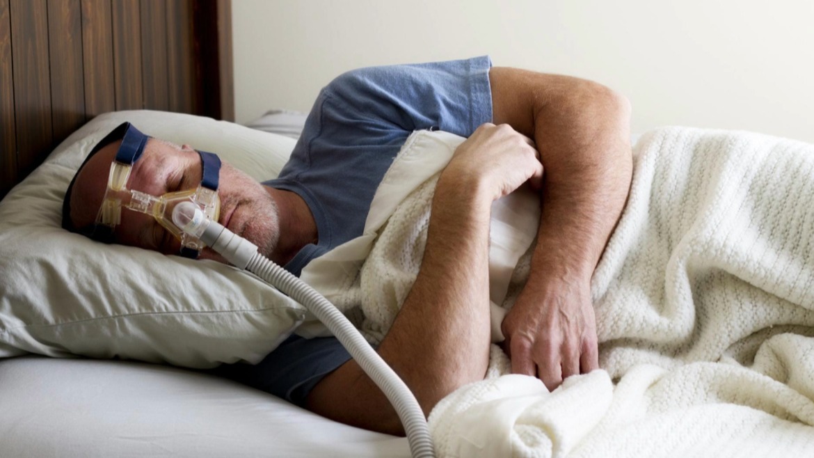 Person sleeping in bed with a CPAP machine for sleep apnea treatment.