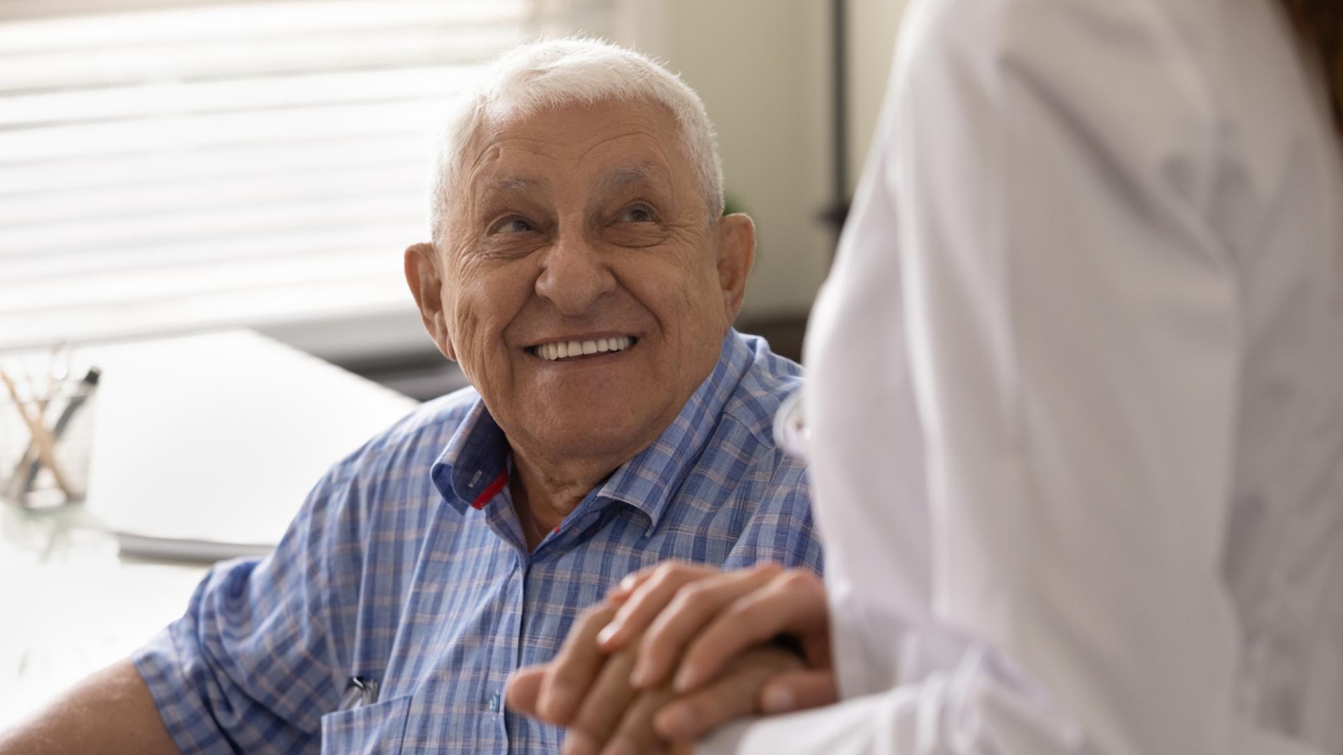 A smiling older man looks up at his doctor.