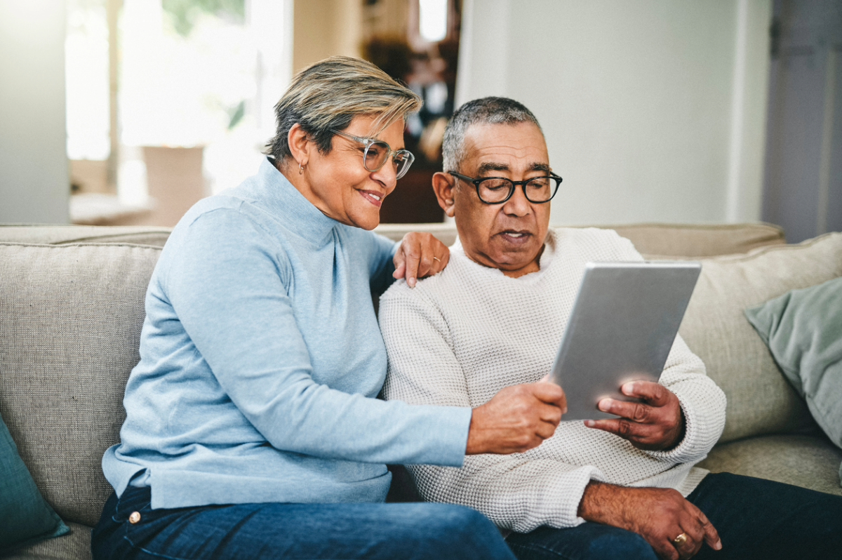 Two older individuals sitting on the sofa using a tablet.