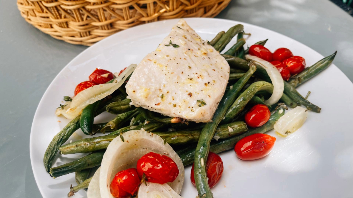 A plate of halibut. The dish is displayed on a white plate with a wicker basket in the background, creating a cozy, homemade feel.