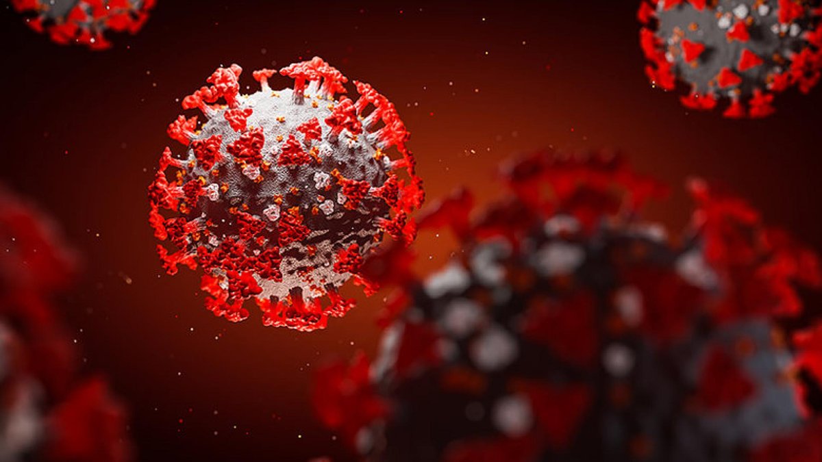 A close-up 3D rendering of the COVID-19 virus, showing the spherical shape covered with red spike proteins on its surface, against a dark background.