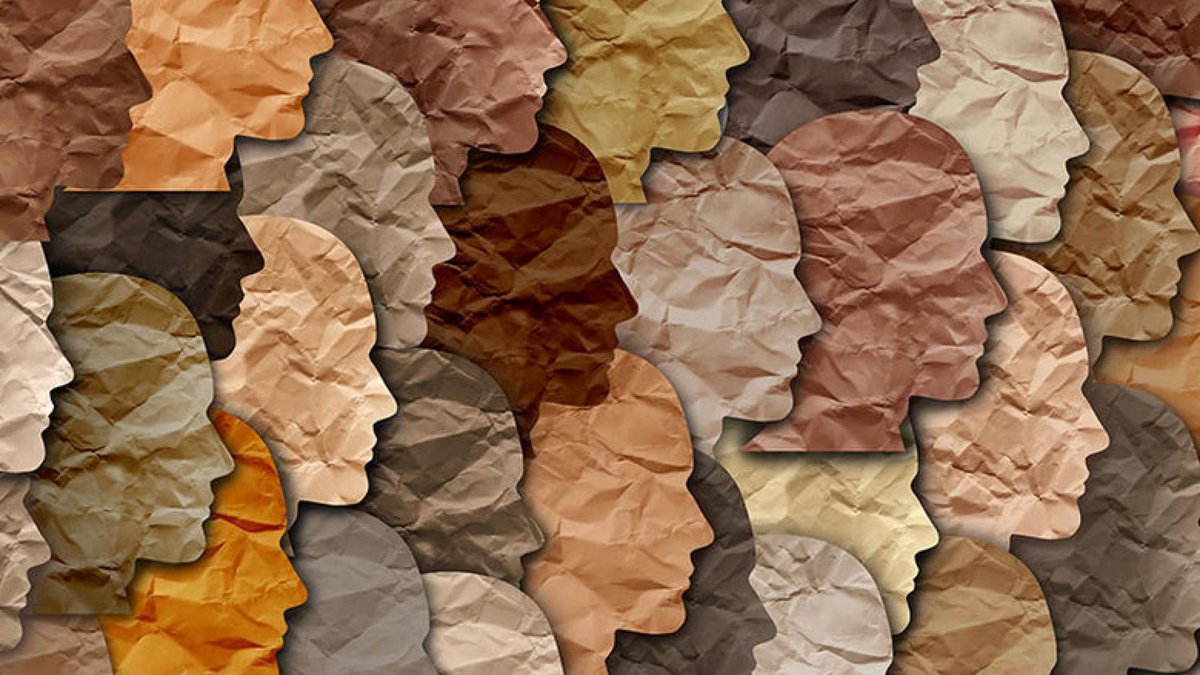 A collage of crumpled paper cutouts in the shapes of human profiles, each in different shades representing a diverse range of skin tones. The image symbolizes diversity and unity.