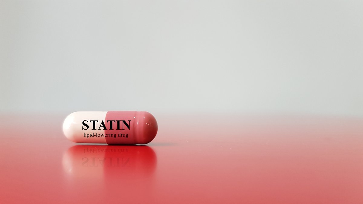 A single capsule labeled "Statin" sits on a reflective surface, representing a lipid-lowering drug used in medical treatments.