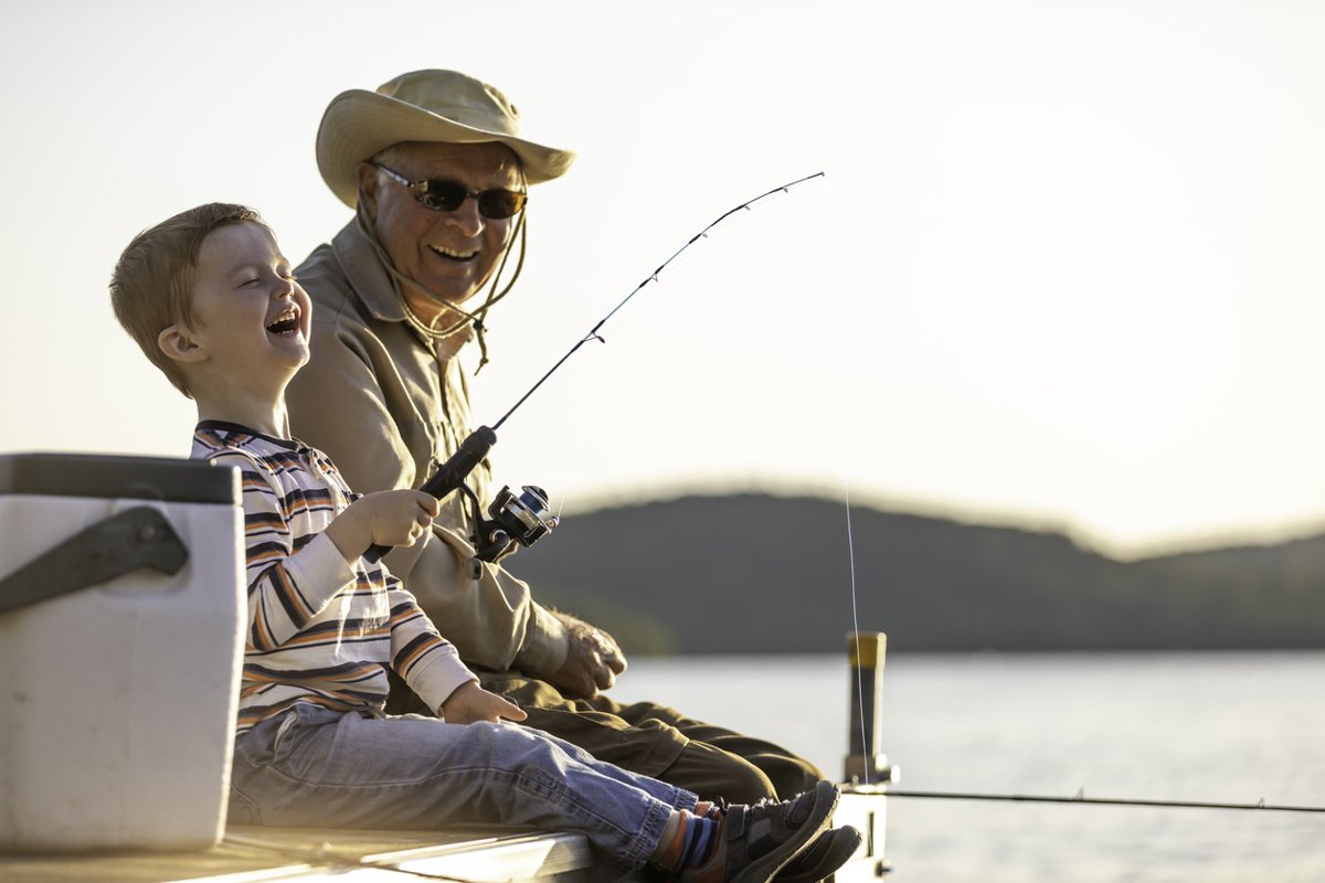 A grandfather and grandson fish on a dock.