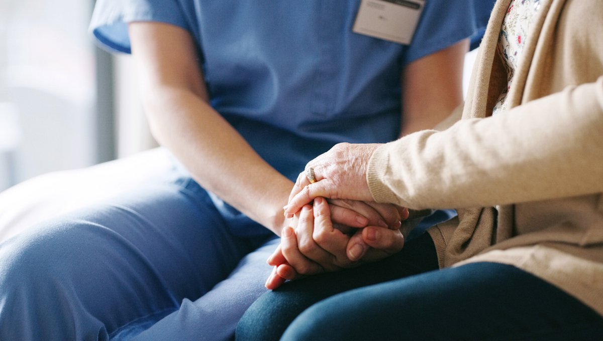 A nurse and a senior woman hold hands.