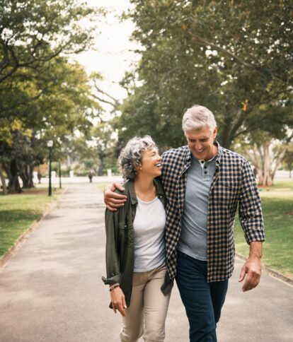 An older couple happily walking arm-in-arm down a park pathway.