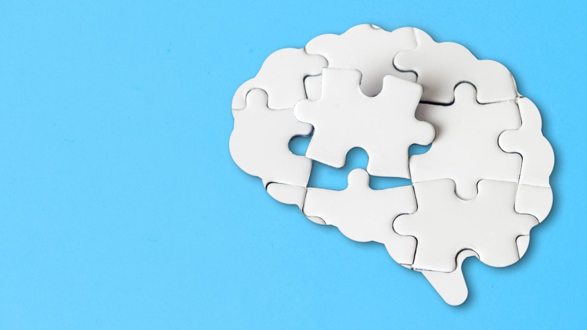 A white puzzle in the shape of a human brain with one missing piece, set against a light blue background, symbolizing cognitive challenges or memory loss.